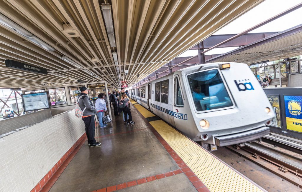 Oakland, California, USA - October 15, 2016: Mixed gender passengers waiting on the platform at MacArthur BART station in Oakland as a train arrives and comes to a halt beside them. The Bay Area Rapid Transport system is designed to alleviate the congestion on the crowded highways on the morning commute to work in the San Francisco area.