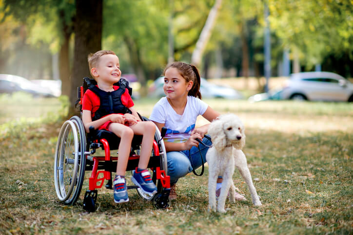 Young boy in wheelchair playing with his sister and dog in the park