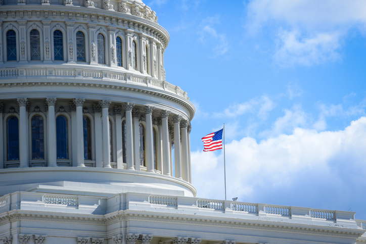 Capitol building in Washington DC, and flag of USA in front. Horizontal photography during bright shinny day, with blue sky in the background