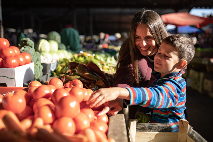A boy is picking out vegetables with his mom at the farmers' market