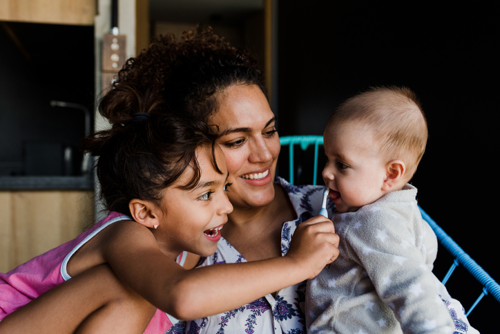 Latin single mother brushing teeth to her baby with daughter at home