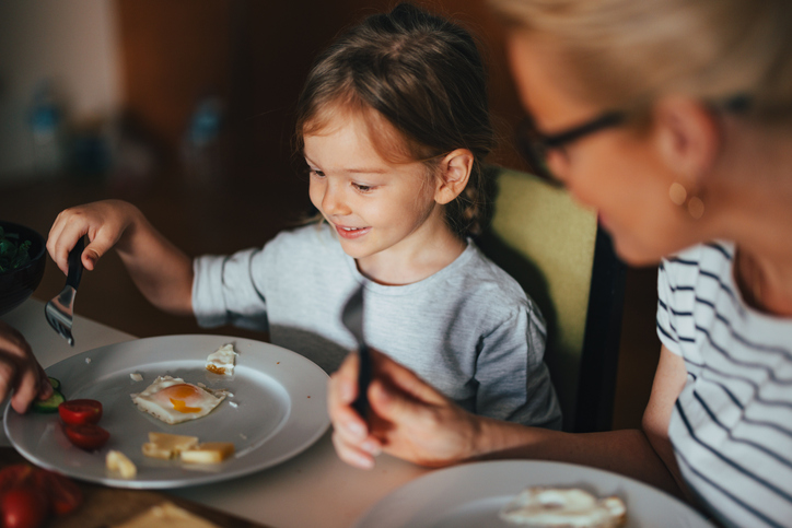 A smiling child having a meal together with her family.
