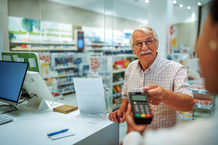 An older man pays for a prescription at a pharmacy counter, representing access to affordable care and the importance of California health coverage for seniors.