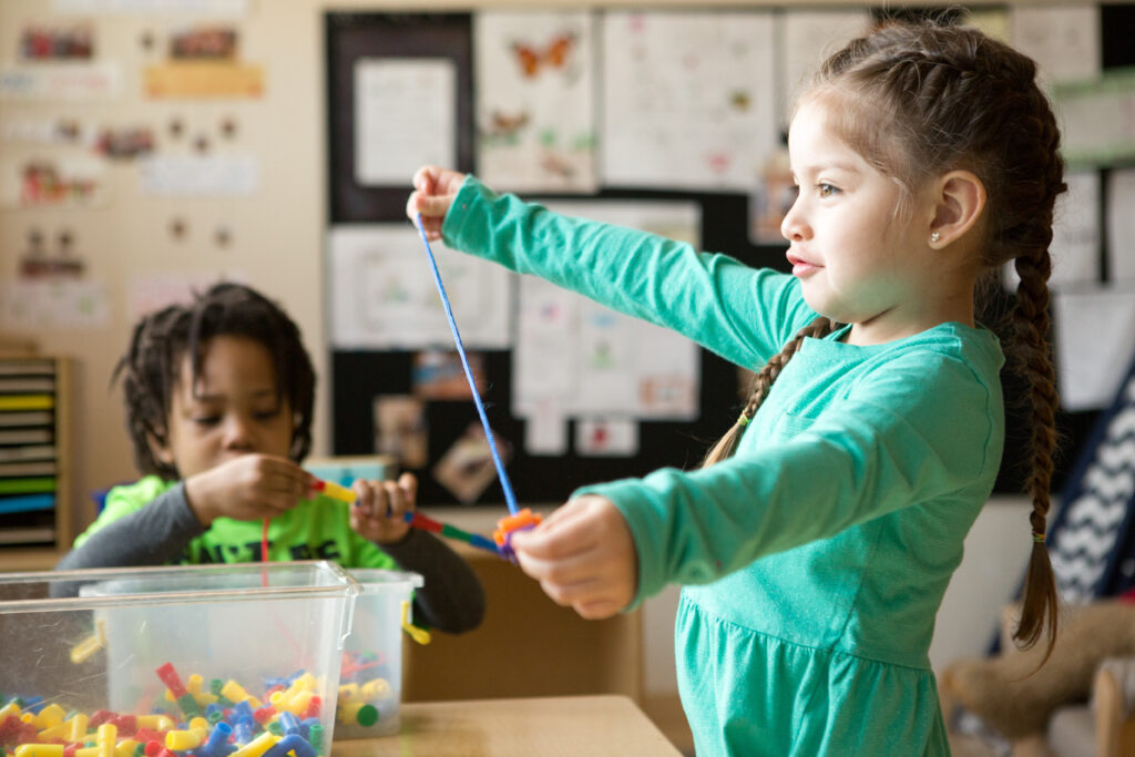 A preschool student threads beads on a string.