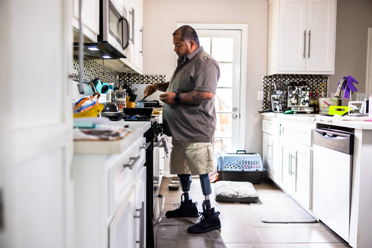 A Hispanic man with two prosthetic legs showcasing his resilience and independence as he confidently prepares breakfast in his kitchen. With a focused expression on his face, he skillfully handles the cooking utensils, demonstrating his ability to overcome challenges and adapt to everyday tasks. The image beautifully portrays determination, strength, and the power of embracing life with a positive spirit.