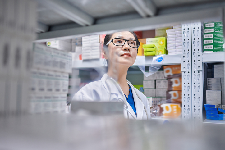 Close-up of one asia female pharmacist using digital tablet while taking inventory at pharmacy warehouse.