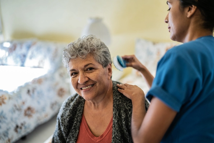 Portrait of a nurse combing senior woman's hair in bedroom at home